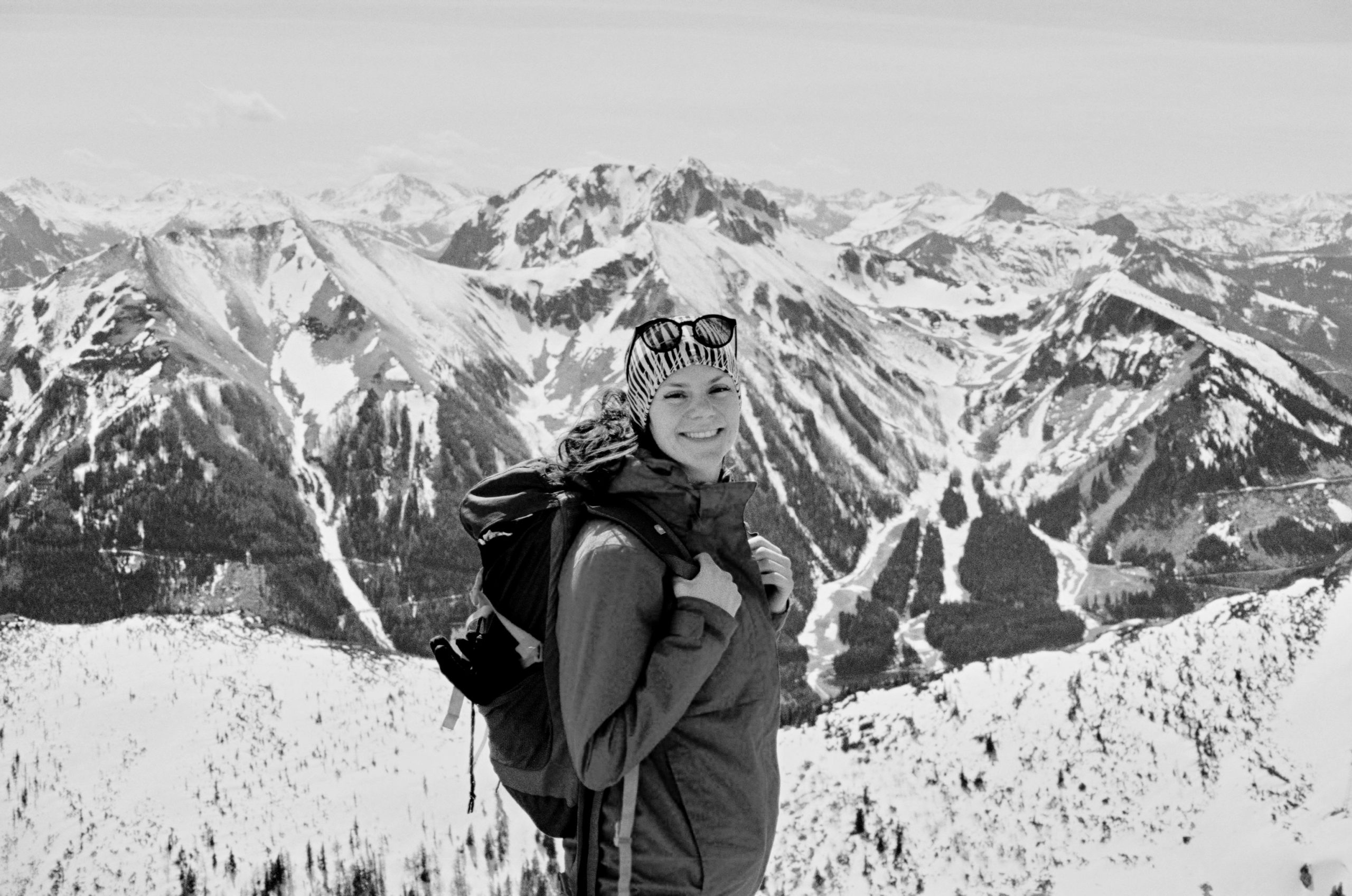 Verschneite österreichische Berglandschaft im Hintergrund, im Vordergrund steht Marina Faffelberger, die Inhaberin vom Übersetzungsbüro HOLA · BONJOUR in Graz, mit einem Rucksack.